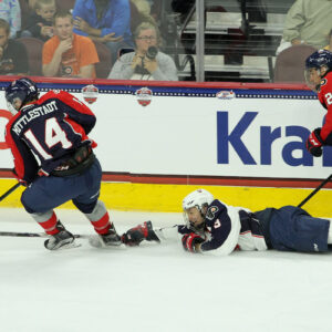 A prone Nate Knoepke (#3 - White) reaches for the puck handled by Casey Mittelstadt (#14 - Blue)